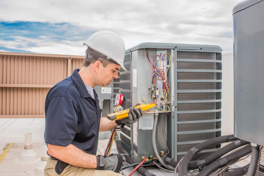 Trained hvac technician holding a voltage meter, performing preventative maintenance on a air conditioning condenser unit.