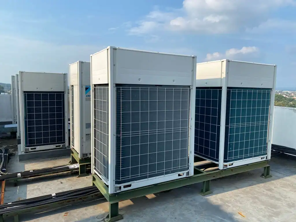 Three large PTAC Air Conditioning & Heating NYC units are installed on a rooftop, with metal pipes and electrical conduits connected to them. The sky is partly cloudy in the background.